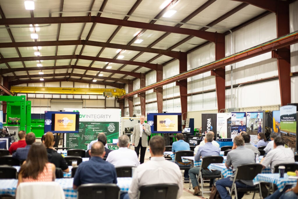 A group of people sit in rows as they listen to a speaker in a large warehouse